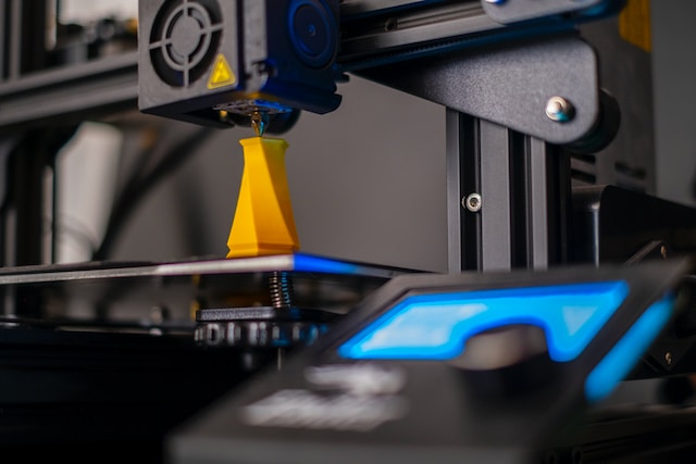 A yellow item is being printed by a 3D printer.