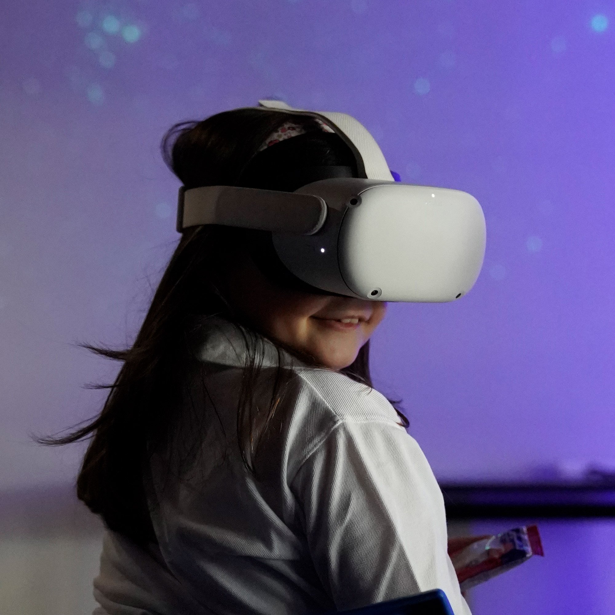 A girl is wearing a VR headset and smiles towards the camera.